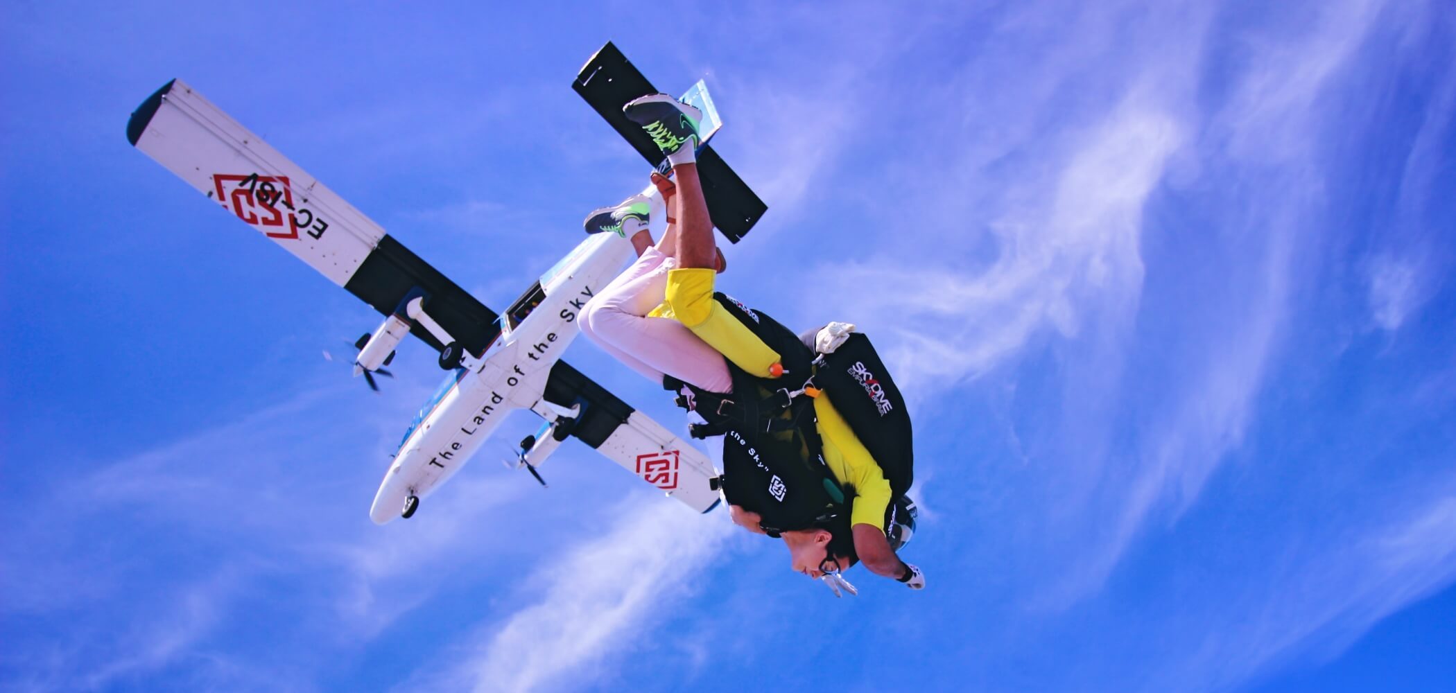 Skydiver in freefall above dramatic landscapes and open skies.