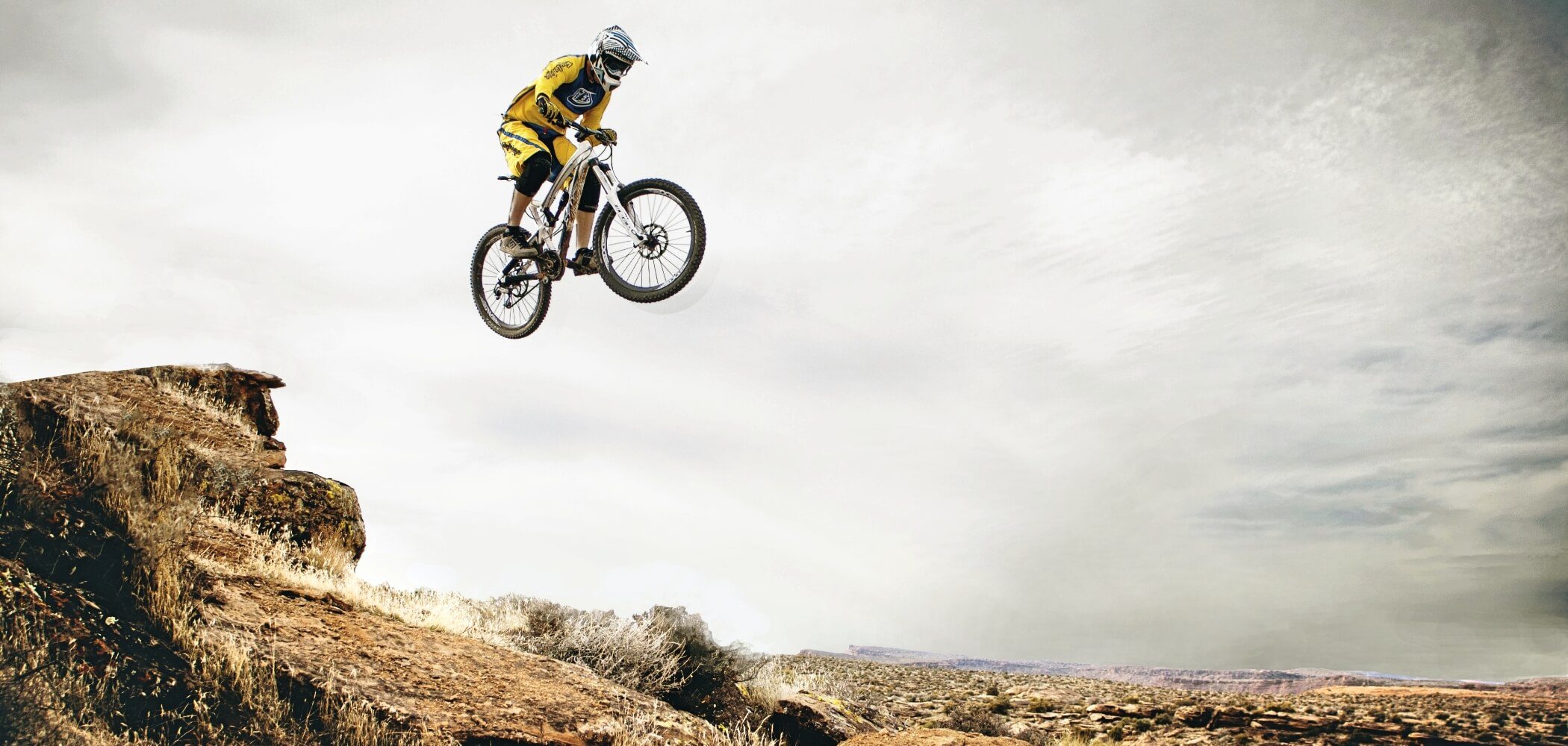 Man performing an aerial bike stunt in a rugged mountain setting.