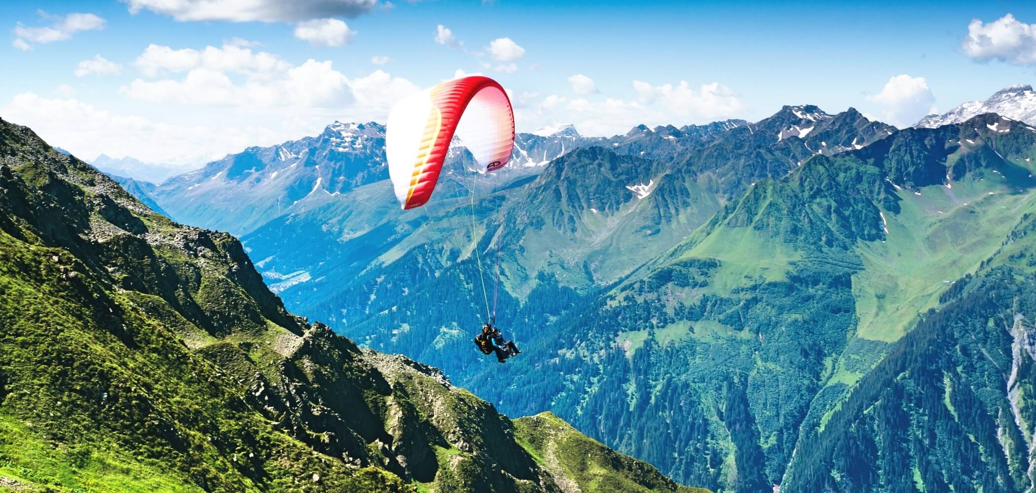 Paraglider soaring above alpine valleys under clear skies.